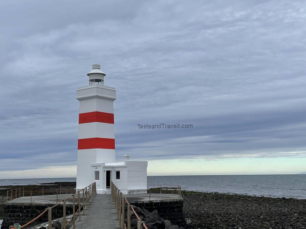 Red and white striped lighthouse on a rocky coast under a cloudy sky in Iceland