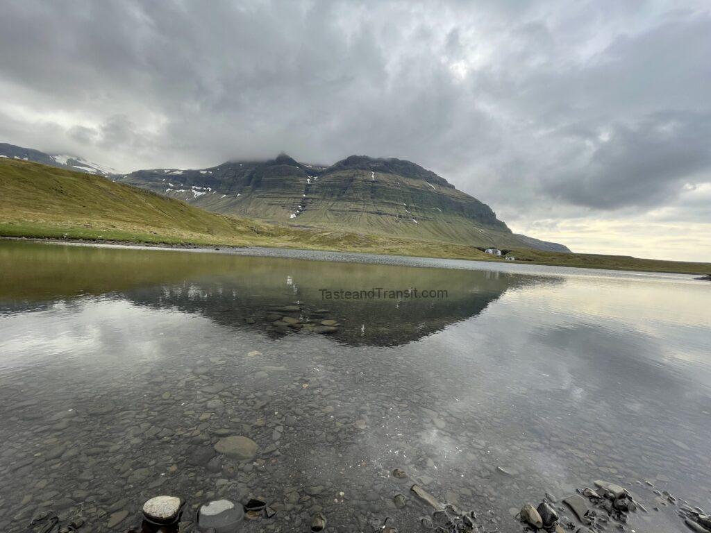 Serene lake reflecting surrounding green hills and cloudy sky in Iceland