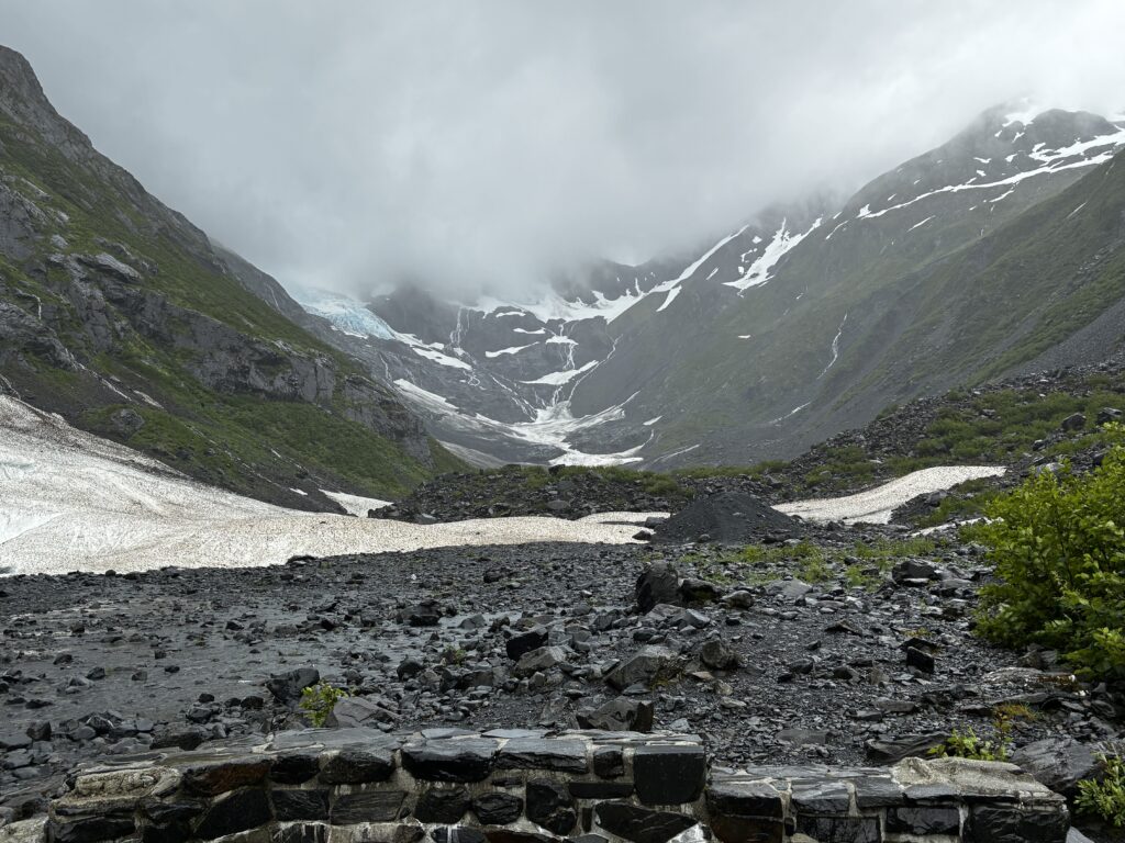 Byron Glacier trail surrounded by rocky terrain and snowy slopes under overcast skies